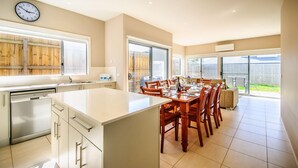 Une cuisine moderne dotée d’un îlot central, d’un coin repas avec des chaises en bois et de grandes fenêtres qui laissent entrer la lumière naturelle.
