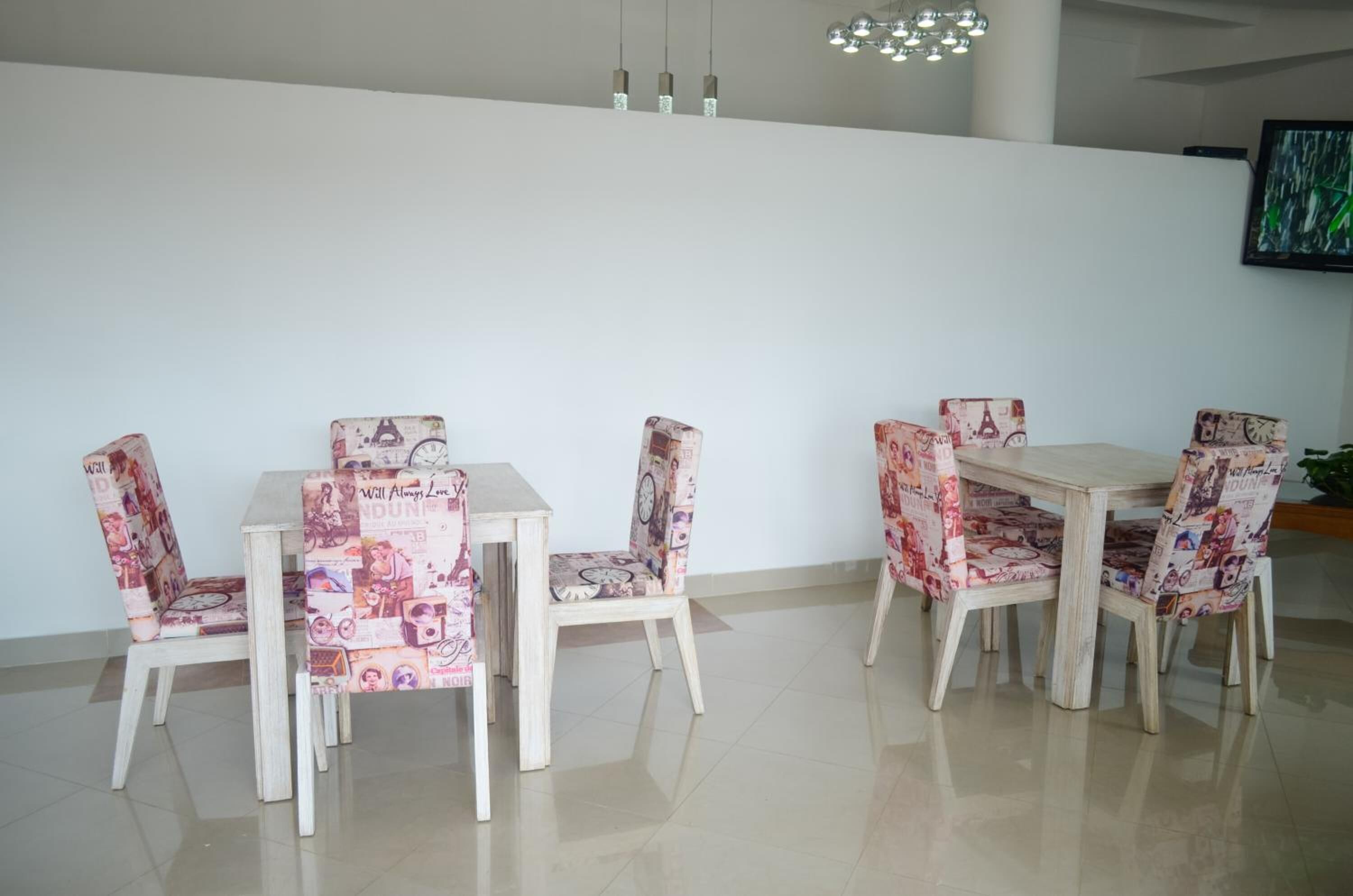 Un comedor con una mesa y sillas blancas, una araña y un cuadro en la pared.