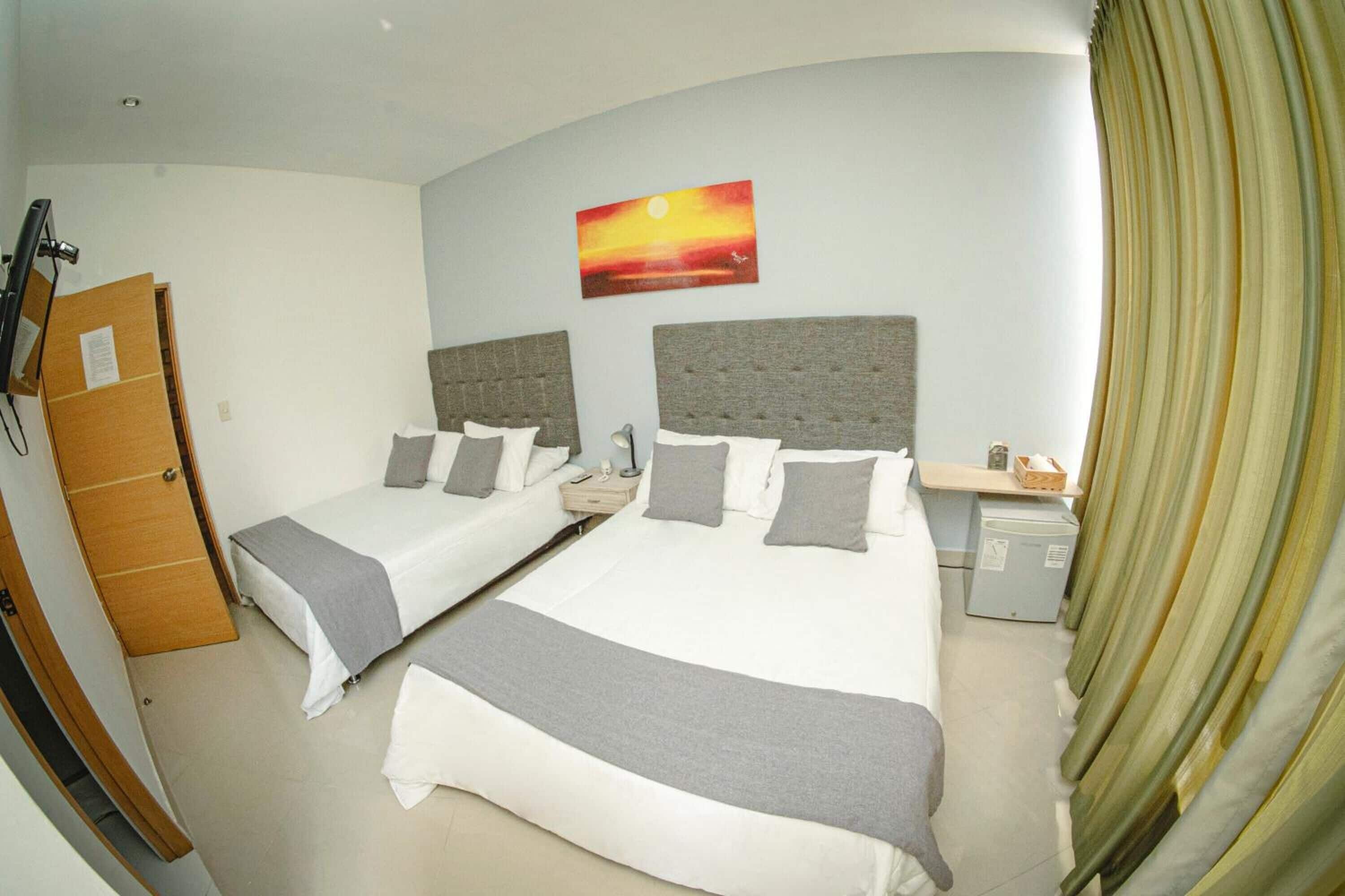 Hotelkamer met twee bedden, een nachtkastje, een bureau, een kleine koelkast en een schilderij van een zonsondergang.