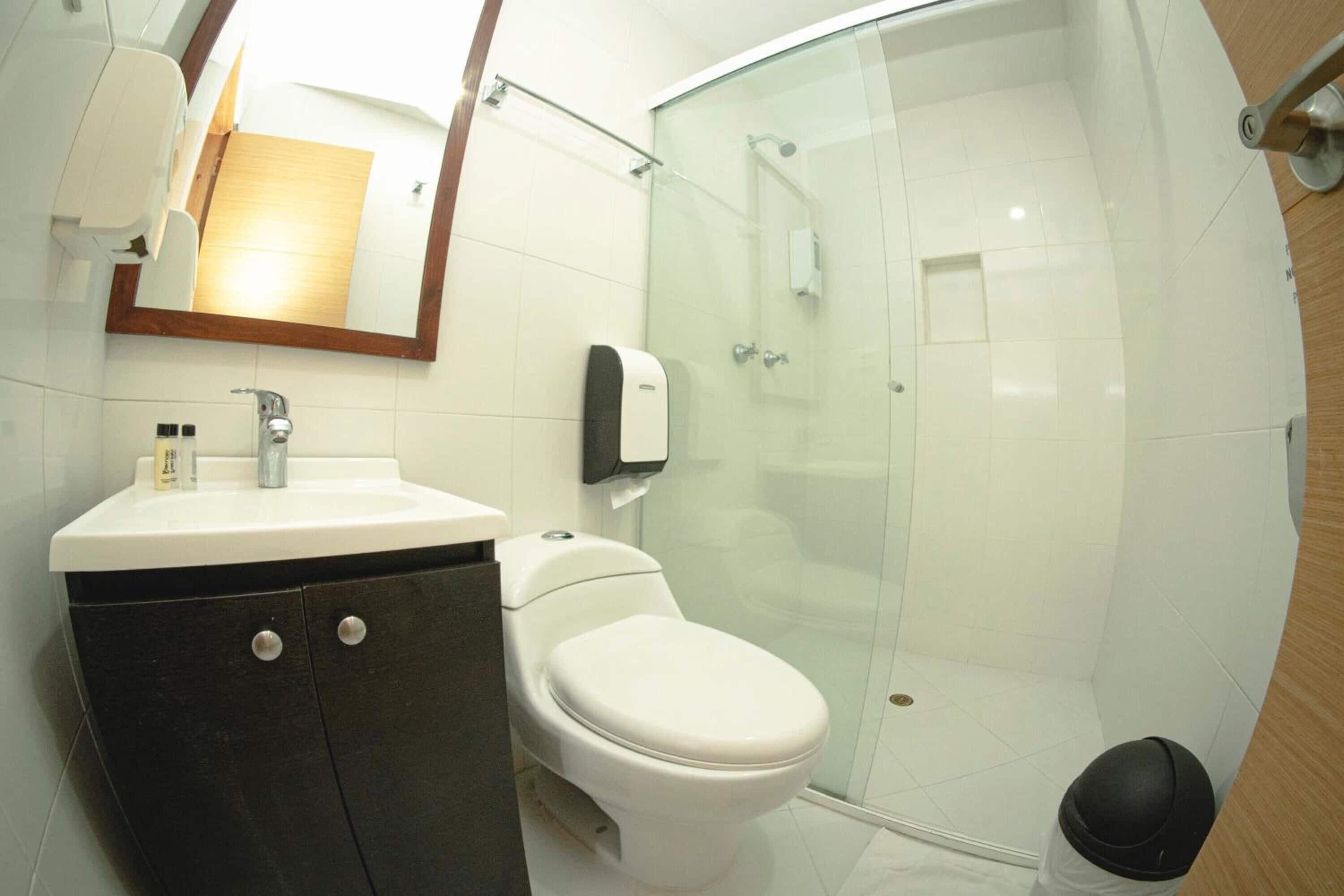 Un baño moderno con inodoro blanco, lavamanos con espejo y zona de ducha con mampara de cristal.