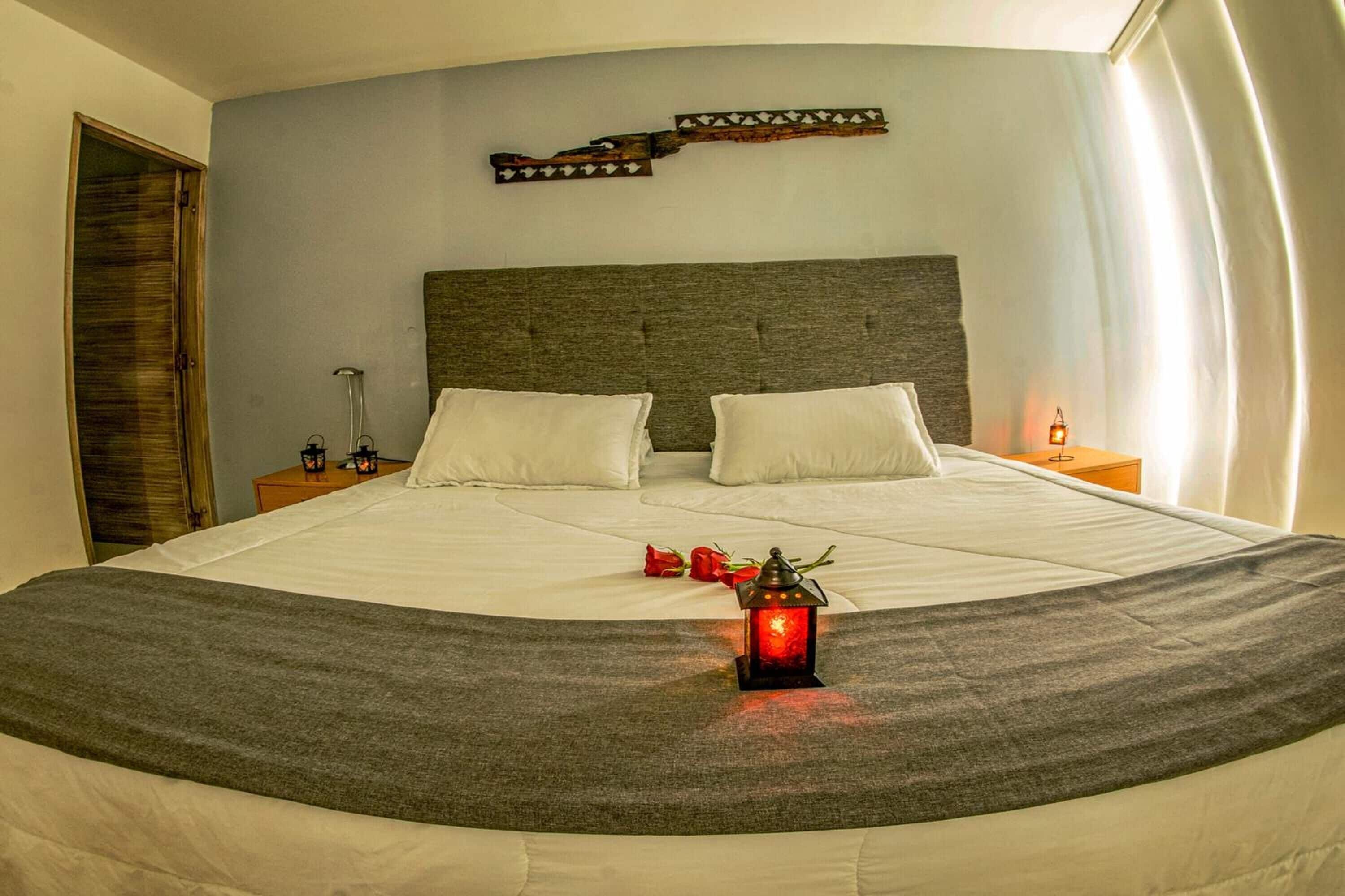 A neatly made bed with white linens, a grey throw blanket, and a decorative lantern on the bed.