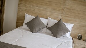 A neatly made bed with white bedding and two gray pillows, a wooden headboard, and a small bedside table with a book and a lamp. - Llanogrande Airport by Bernalo Hotels (Rionegro)