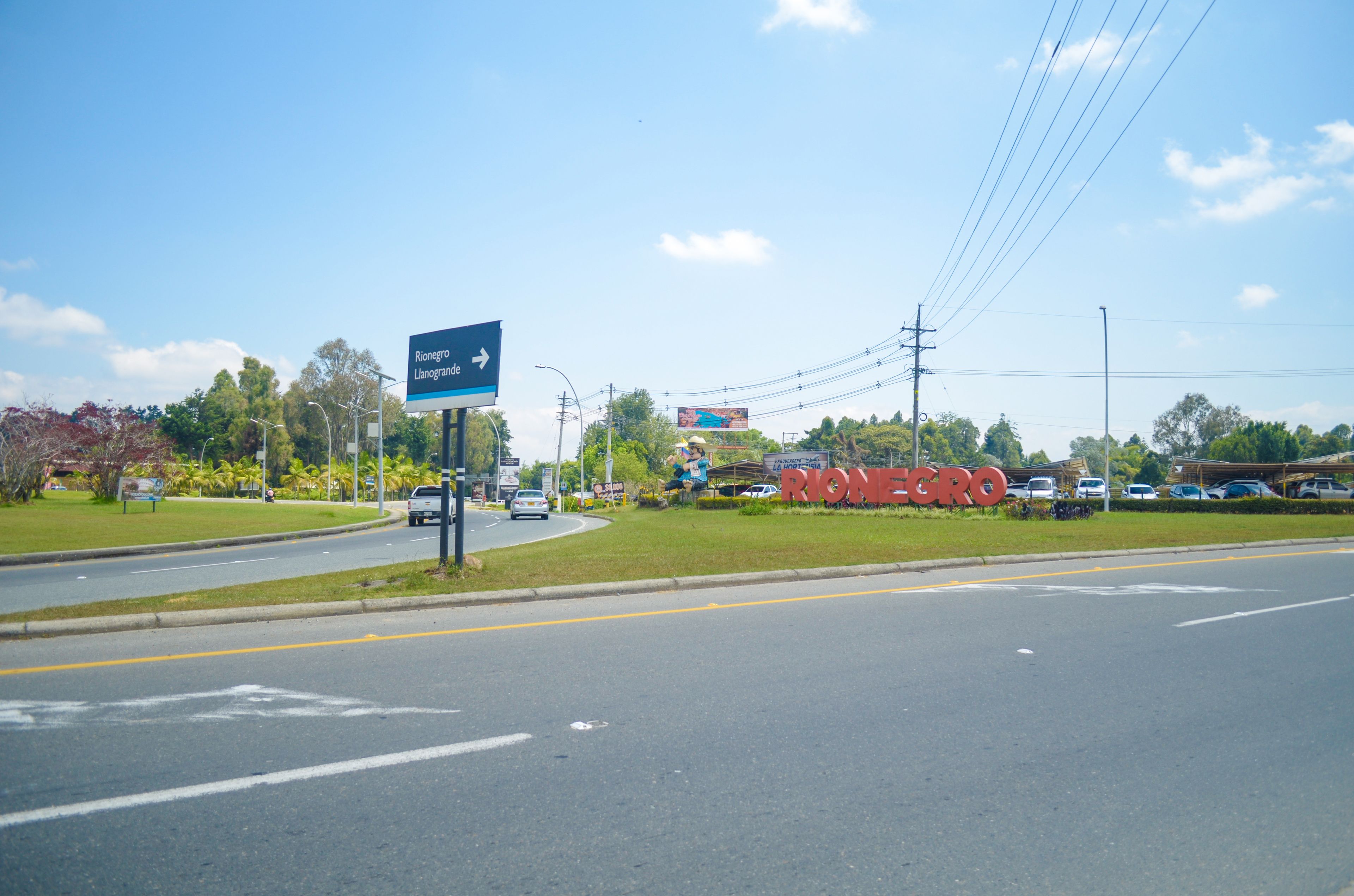 A road with a blue directional sign and a large red sign for Rionegro.