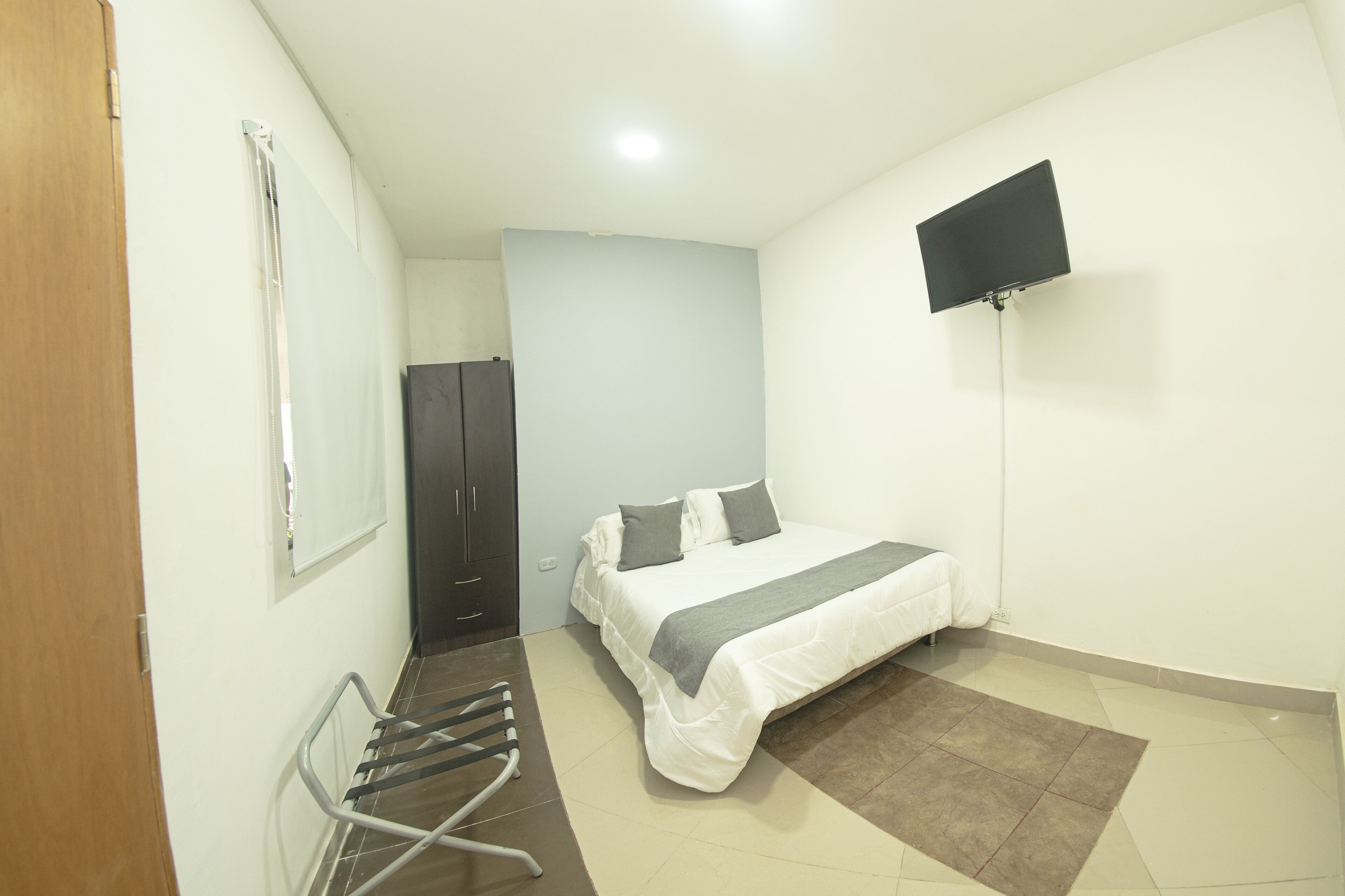 Une chambre à coucher avec un lit, un téléviseur fixé au mur, une porte et une fenêtre.