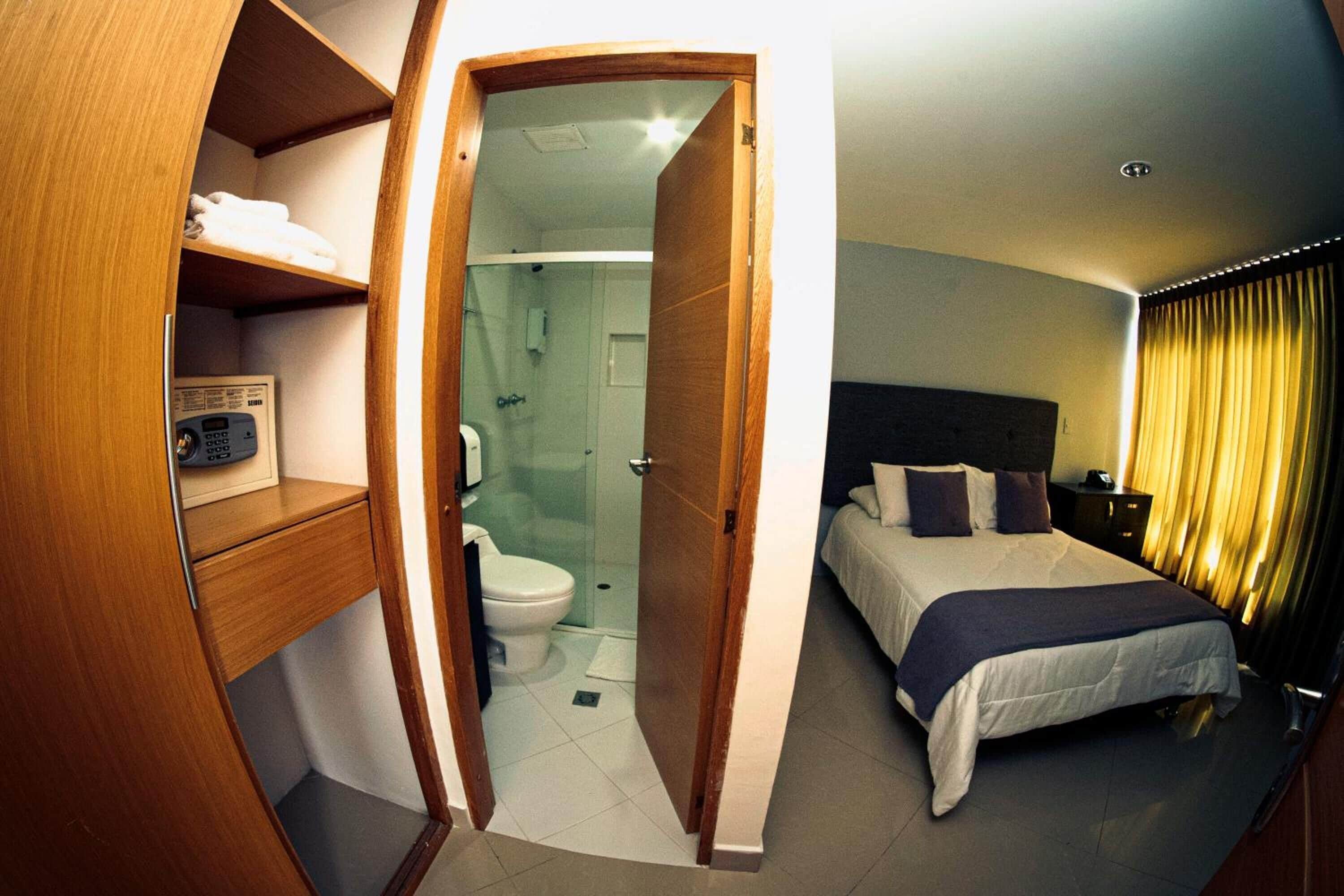 A hotel room with a wooden wardrobe, a shower, a bed with a headboard, and a bedside table.