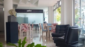 A modern lobby with a black leather sofa, a glass coffee table, and a tiled wall with a geometric pattern. There are several chairs with floral tablecloths and a large window providing natural light. - Llanogrande Airport by Bernalo Hotels (Rionegro)