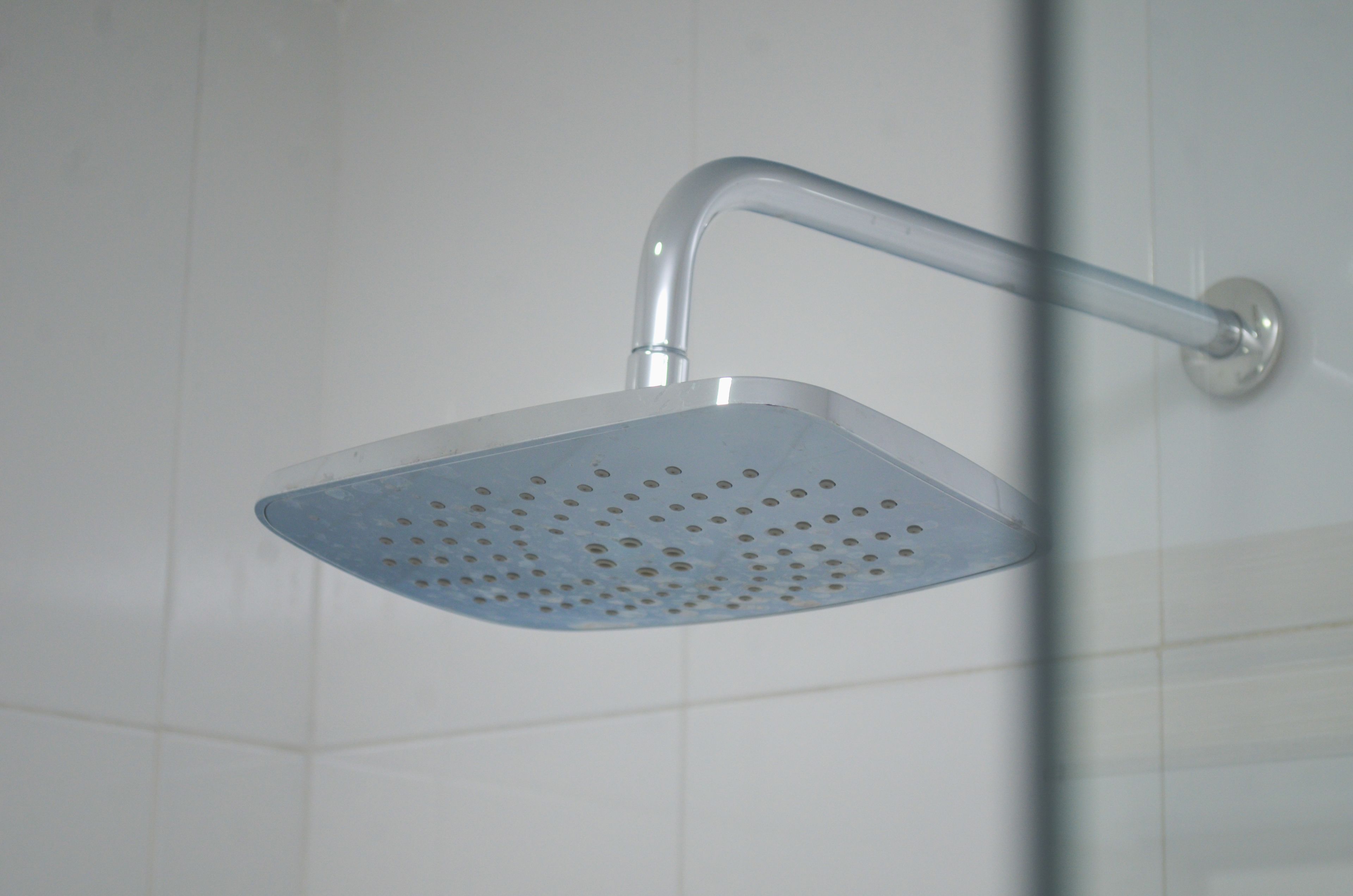 A modern showerhead with a curved design, mounted on a wall with white tiles.