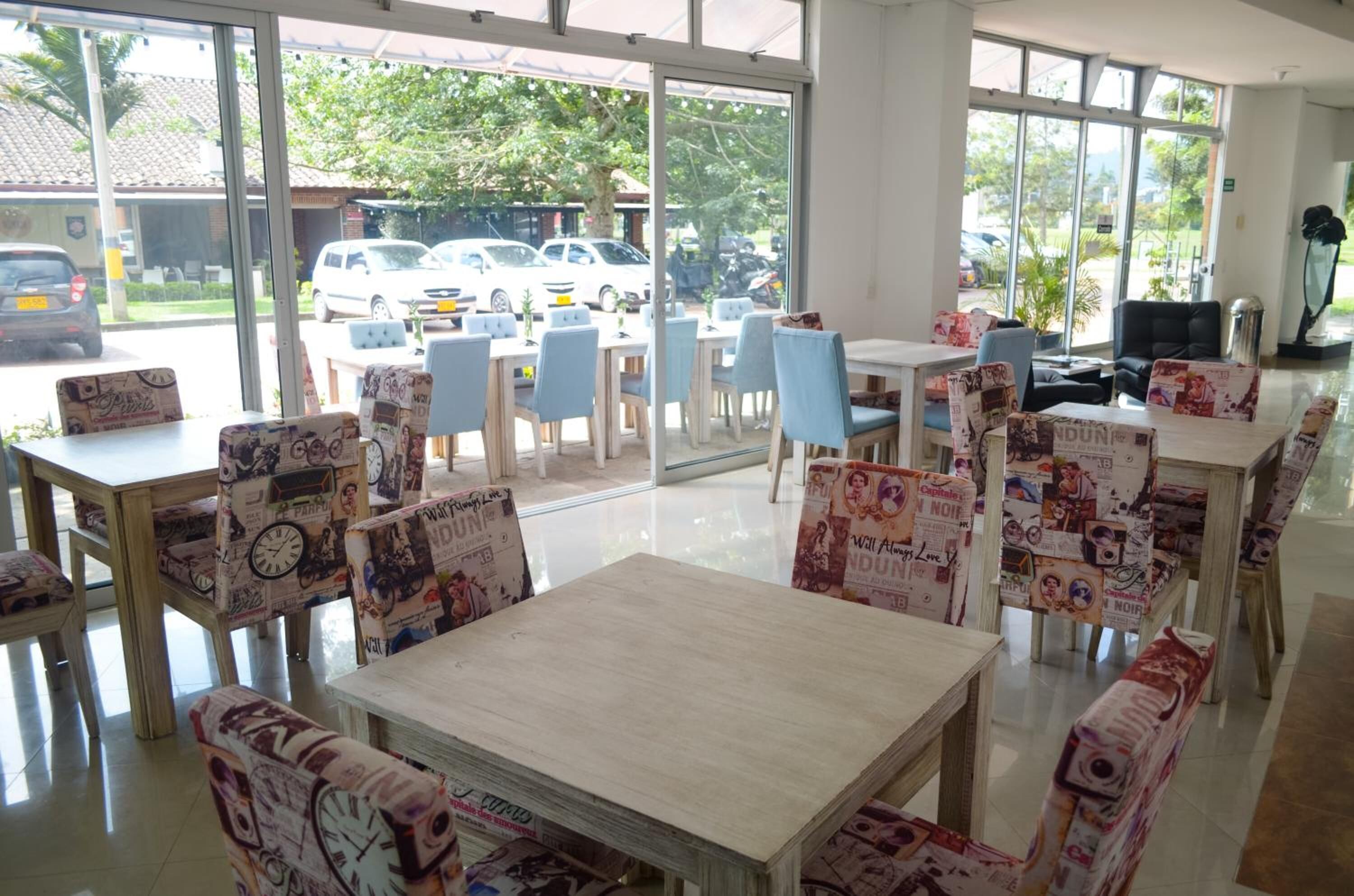 Um restaurante com mesas, cadeiras, janelas amplas e vista para carros estacionados na rua.