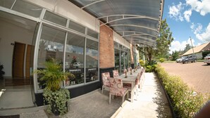 An outdoor seating area with tables and chairs, a covered walkway, and a view of a building with large windows and a sign that reads "Abierto". - Llanogrande Airport by Bernalo Hotels (Rionegro)