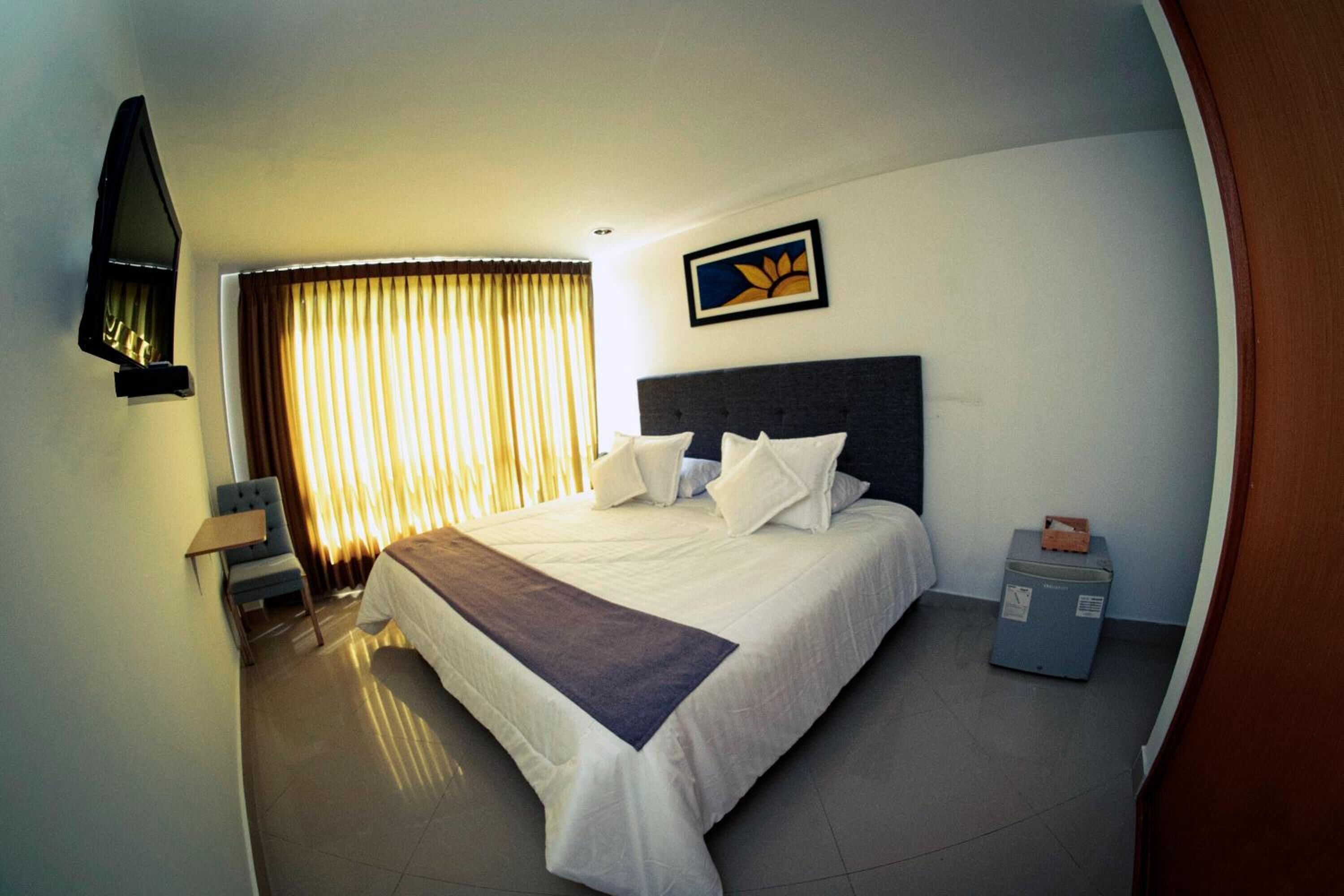 Quarto de hotel com uma cama grande, televisão de tela plana na parede, escrivaninha com cadeira e janela com cortinas.