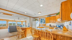 A spacious kitchen with wooden cabinets, a central island, and a dining area with wooden chairs. - Oceanfront Dog Friendly Cottage in Avon with Grill and Screened Porch (Avon)