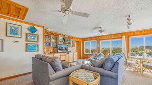 A cozy living room with two grey sofas, a glass-top coffee table, and a bookshelf filled with books. - Oceanfront Dog Friendly Cottage in Avon with Grill and Screened Porch (Avon)