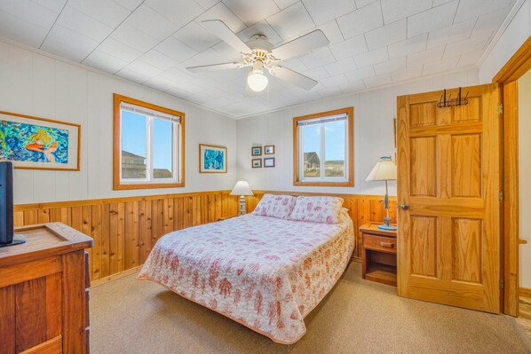 Une chambre à coucher avec un lit, des murs en bois, un ventilateur de plafond et une porte.