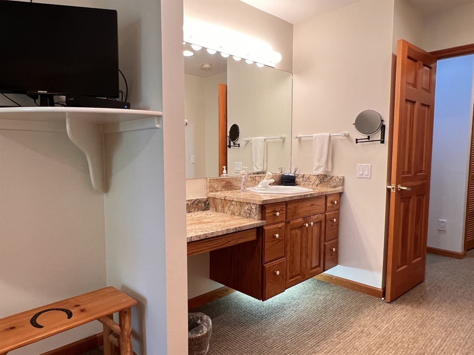 A bathroom with a vanity, mirror, and a television mounted on the wall.