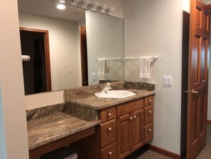 A bathroom with a granite countertop, a white sink, wooden cabinets, a large mirror, and a towel rack.