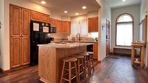 A kitchen with wooden cabinets, a black refrigerator, a sink, and a bar area with stools.