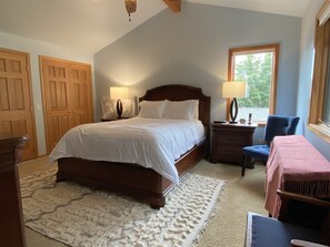 A bedroom with a large bed, two bedside tables with lamps, a chair, a window, and a door.