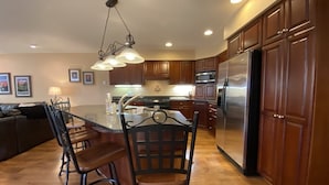 A modern kitchen with wooden cabinets, a stainless steel refrigerator, and a central island with bar stools.