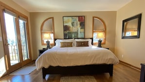 A bedroom with a large bed, two bedside lamps, a rug, and a painting on the wall.
