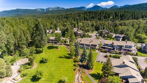 A residential area with multiple houses, a large lawn, and a forested backdrop. - Mountain Harbor #143 3 Bedroom Condo (Whitefish)