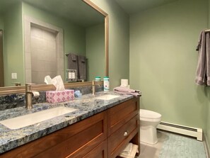 A bathroom with a marble countertop, a wooden vanity, a white toilet, and a large mirror. - Mountain Harbor #143 3 Bedroom Condo (Whitefish)