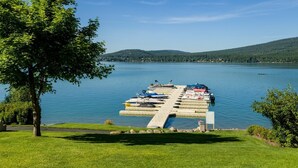 Un muelle con barcos, un área verde y un lago con colinas al fondo.