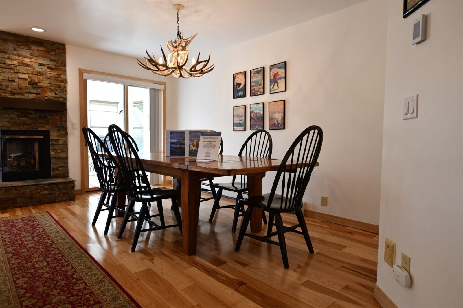 A dining area with a wooden table and chairs, a stone fireplace, and a chandelier.