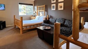 A bedroom with a wooden bed, a sofa, a small table, and a window. - Mountain Harbor #127 2 Bedroom Condo (Whitefish)