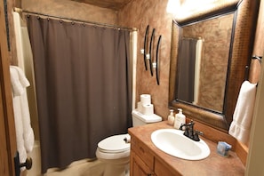A bathroom with a shower curtain, toilet, sink, and mirror. - Mountain Harbor #127 2 Bedroom Condo (Whitefish)