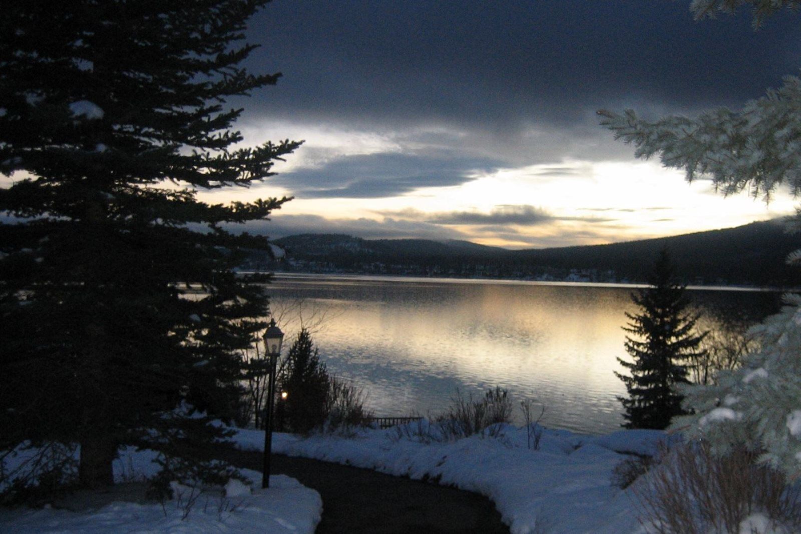 A serene lake at dusk with snow-covered ground and trees, reflecting the sky.
