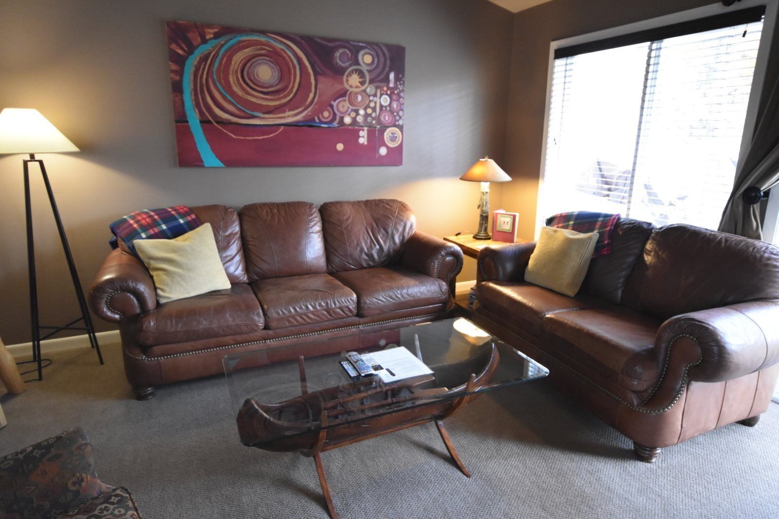 A living room with two brown leather sofas, a glass coffee table, and a large abstract painting on the wall.