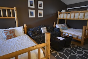 A room with two bunk beds, a sofa, and a small table. There are four framed pictures on the wall. - Mountain Harbor #127 2 Bedroom Condo (Whitefish)