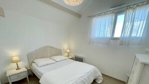 A bedroom with a bed, two bedside tables with lamps, a radiator, and a window with curtains. - Joli Appartement avec terrasse face à l'océan (016) (Biscarrosse)