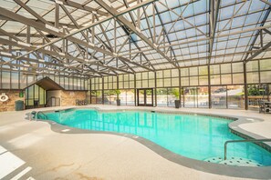 An indoor swimming pool with a glass ceiling, surrounded by a concrete floor and a brick wall.
