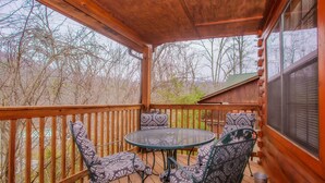 A wooden deck with a round table and four patterned chairs, surrounded by a wooden railing. - 🌲Dancing Bear Den🌄Mountain Views, Resort Pool & Hot Tub (Sevierville)