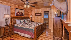 A wooden-paneled bedroom with a bed, a ceiling fan, a mounted deer head, and a painting of pottery. - 🌲Dancing Bear Den🌄Mountain Views, Resort Pool & Hot Tub (Sevierville)