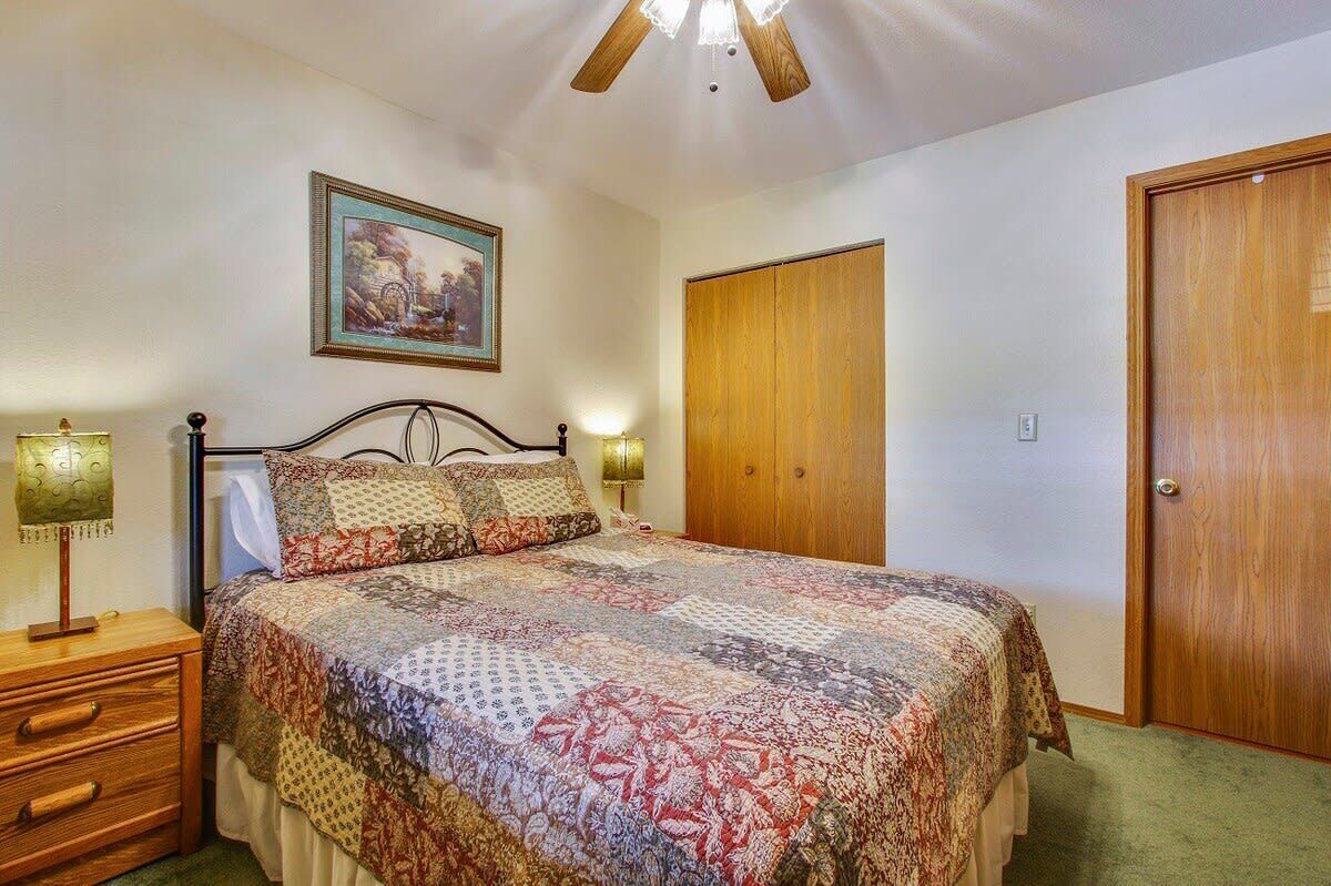 Un dormitorio con cama, lámparas de noche, una puerta de madera y un ventilador de techo.