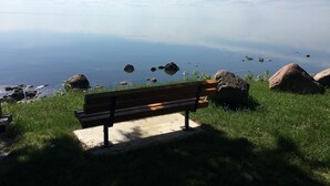 Un banco con vistas a una masa de agua tranquila, rocas dispersas y cielo despejado.