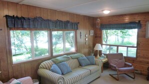 Una habitación acogedora con un sofá a rayas, un sillón mecedor y una ventana con vistas a árboles.