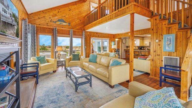 A spacious living room with a high ceiling, wooden walls, and large windows offering a view of the outdoors. - Oceanfront Avon Home w/ Hot Tub, Foosball, Community Pool and Tennis/Pickleball (Avon)