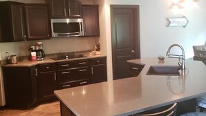 A modern kitchen with dark wood cabinets, a stainless steel microwave, and a large island with bar stools. - Close to Aquatic Center, Horicon Marsh, Wedding Venue, Easy Drive to EAA (Waupun)