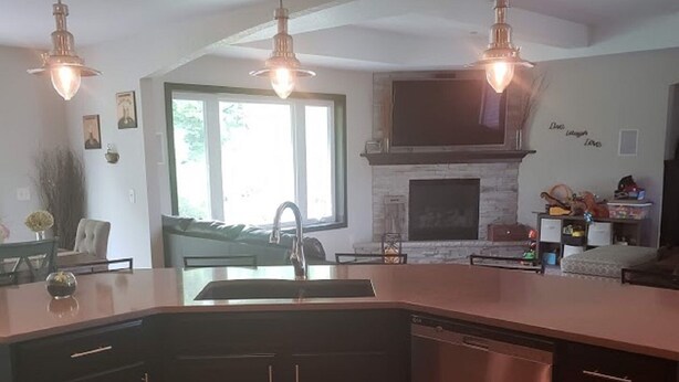 A modern kitchen with a large island, stainless steel appliances, pendant lighting, and a stone fireplace. - Close to Aquatic Center, Horicon Marsh, Wedding Venue, Easy Drive to EAA (Waupun)