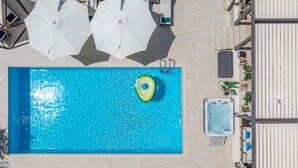 En vy från ovan av en swimmingpool med ett bubbelbad, vita parasoller och solstolar.