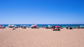 Ein Strand mit vielen bunten Sonnenschirmen und entspannten Menschen im Sand.