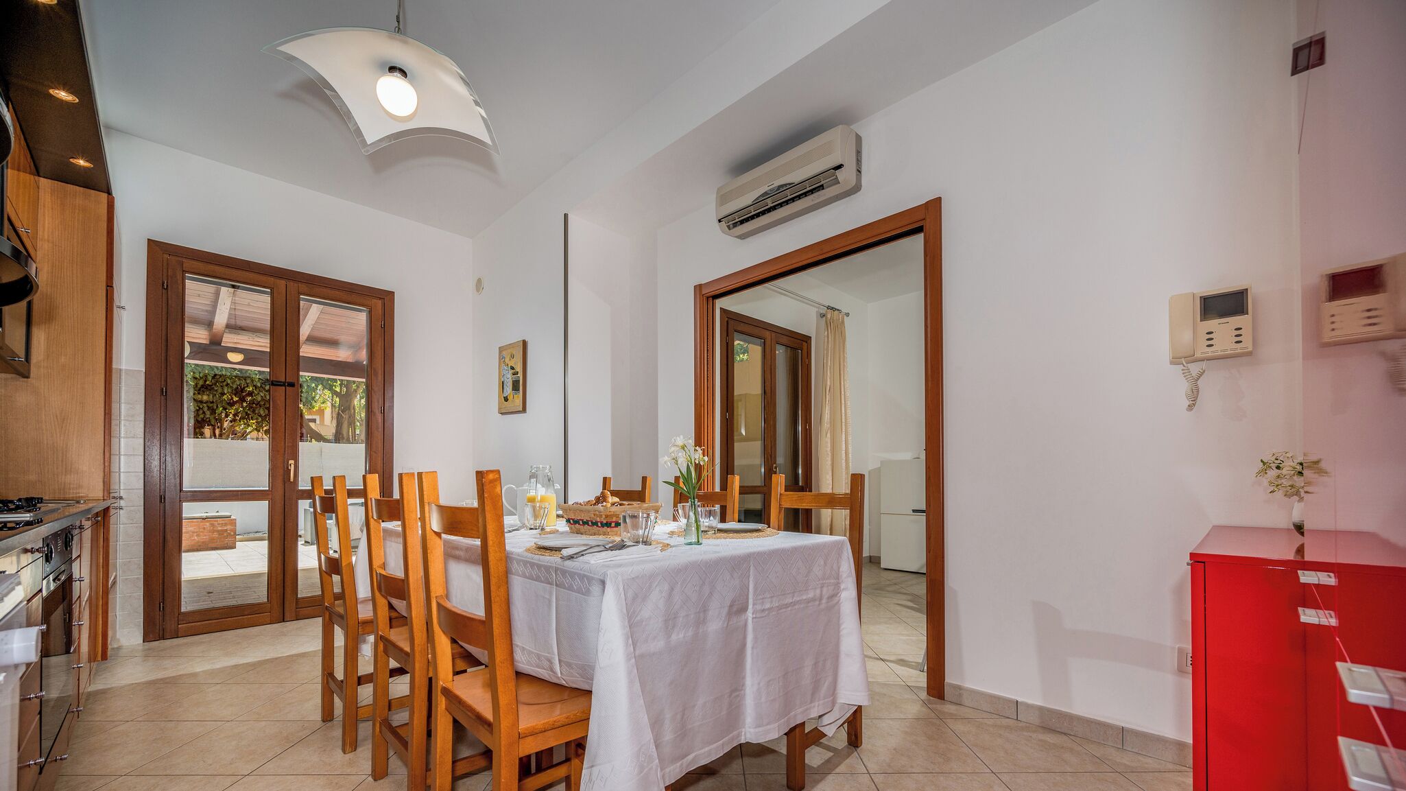 A dining area with a table set for four, wooden chairs, a white tablecloth, and a ceiling light fixture.