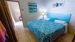 Un dormitorio con cama, mesita de noche, lámpara y un cuadro en la pared.