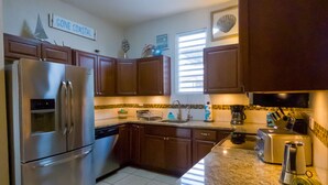 Una cocina con armarios de madera, un refrigerador de acero inoxidable, un lavamanos y una ventana con persianas.