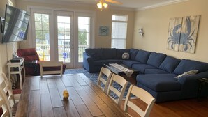 Un salon avec un canapé d’angle bleu foncé, une table à manger en bois et un téléviseur fixé au mur.