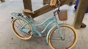 Un vélo ancien, doté d’un panier et d’une selle, est garé sous une structure en bois.