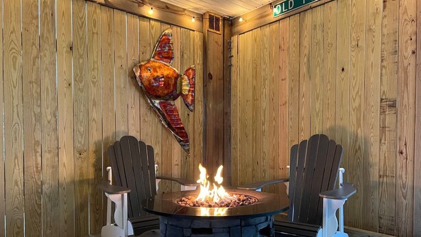 Une pièce chaleureuse avec un foyer en pierre, deux fauteuils Adirondack, des murs en bois et une grande décoration représentant un poisson.